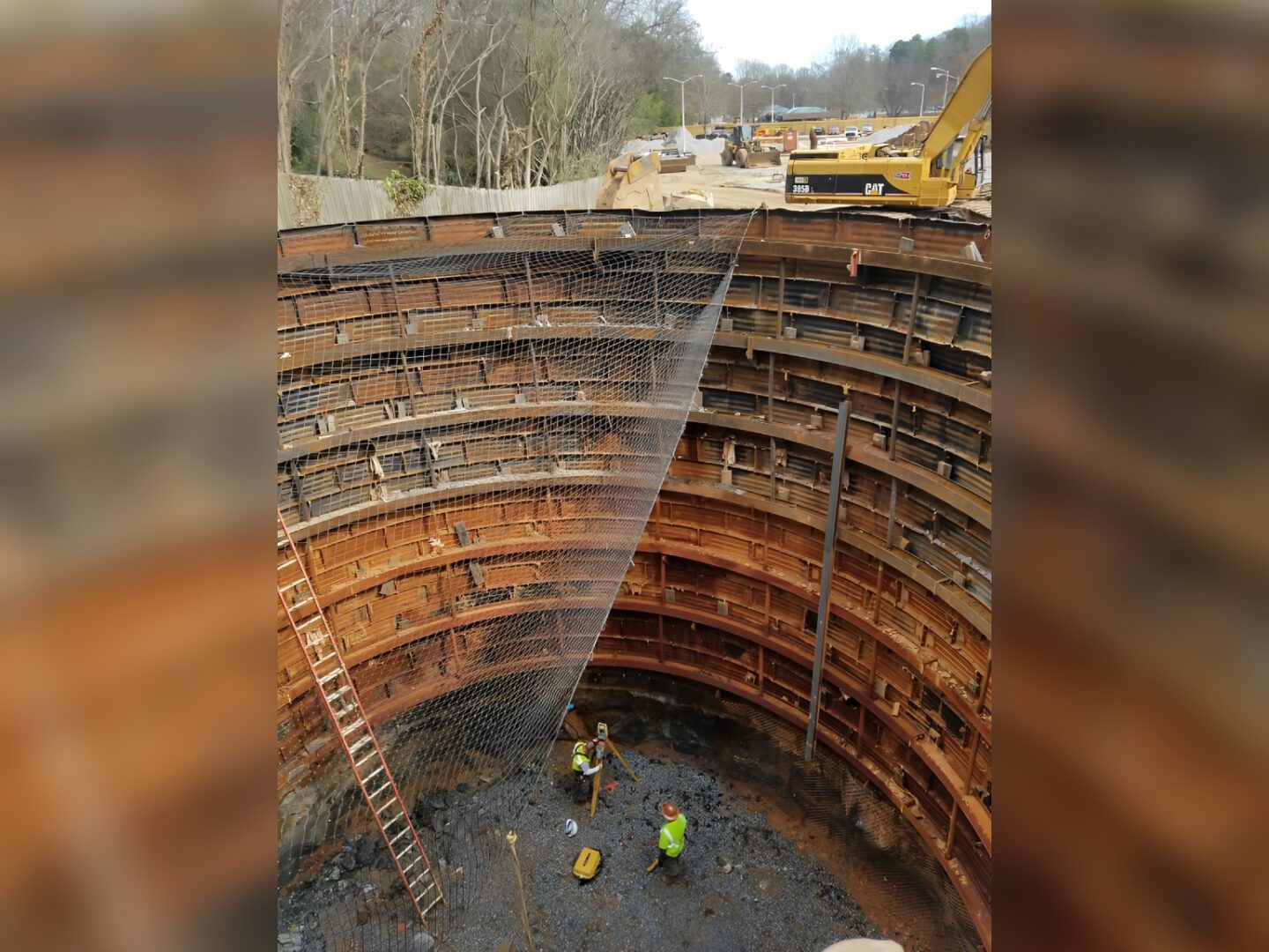 Deep construction pit with workers and machinery.