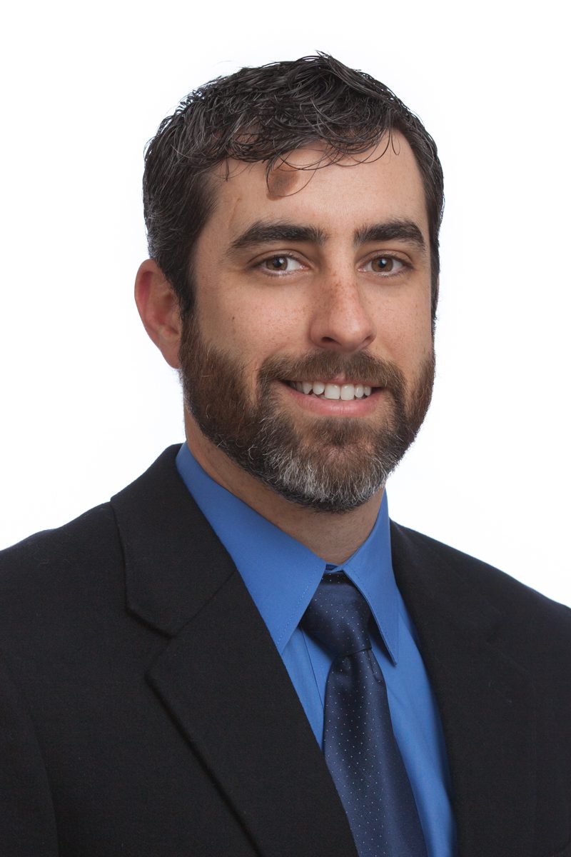 Professional man in suit with blue shirt and tie smiling.