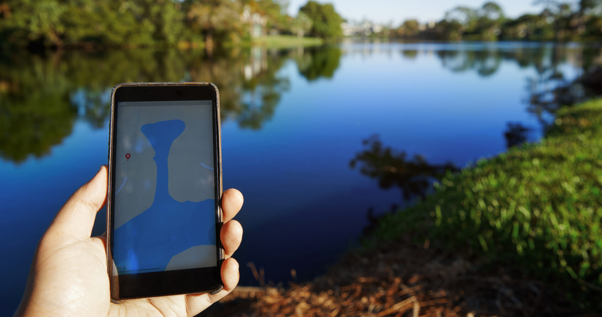 Hand holding smartphone by a serene lake.
