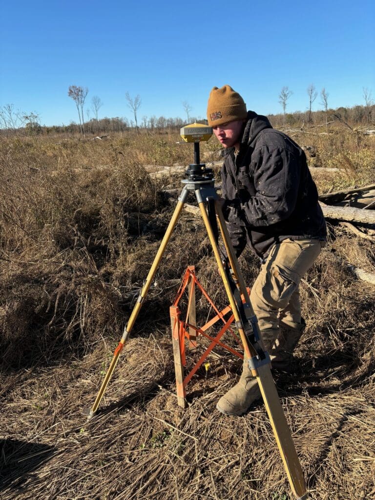 Surveyor using equipment in a field.
